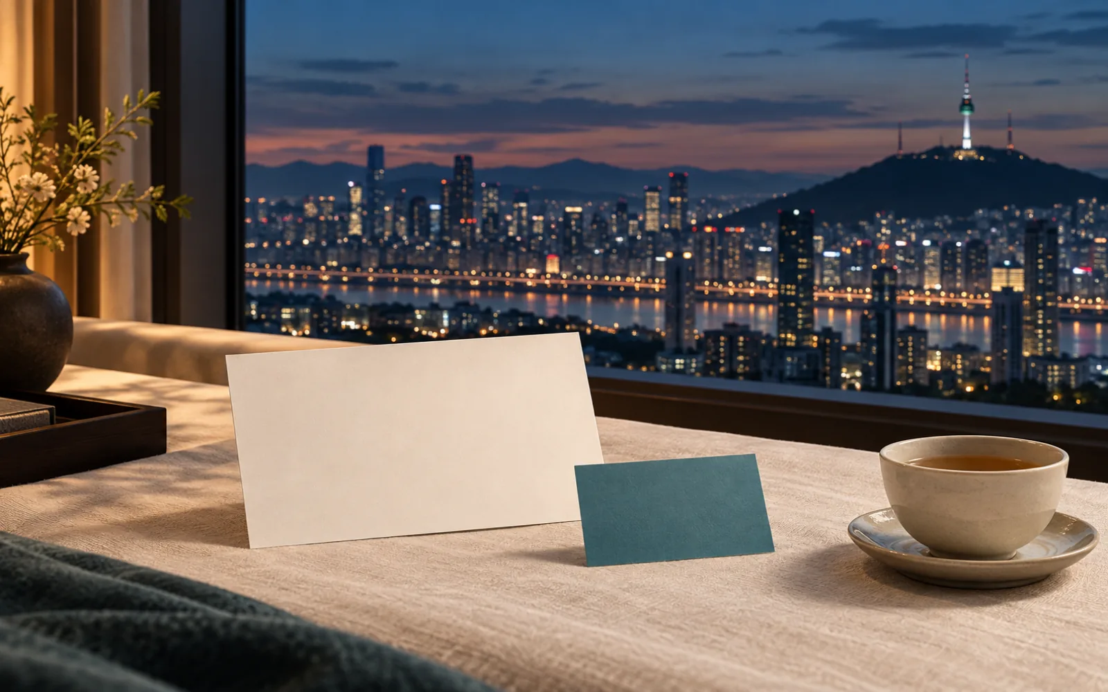 A quiet Seoul hotel window at dusk with blank itinerary cards and tea on linen